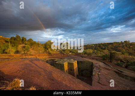 Rainbow set against a grey stormy sky, as golden sunset light catches the top of the ancient stone-carved Bet Giyorgis (Church of St. George), Lalibela, Ethiopia Stock Photo