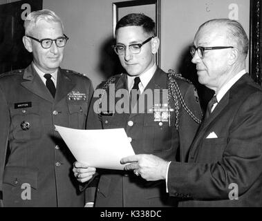 Milton Stover Eisenhower, President of Johns Hopkins University, stands to present the Distinguished Military Student Award to James Hemsley, wearing uniform and holding paper certificate, next to Major General Frank H Britten in uniform to his right, all three men wearing glasses, Baltimore, Maryland, 1965. Stock Photo