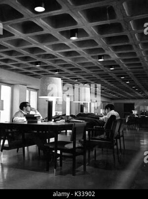 On an underground study and reading level inside the Milton S Eisenhower Library at Johns Hopkins University, male students sit at tables reading books beside lamps, their blazers resting on top of the tables, in a quiet, dimly lit space, Baltimore, Maryland, 1965. Stock Photo