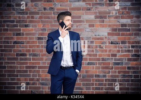 A photo of young man in navy suit. He's talking on the mobile. Stock Photo