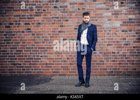 A photo of young man in navy suit and shawl. He's standing in front of the brick wall. Stock Photo