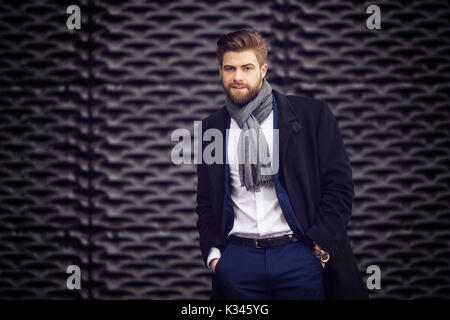 A photo of young, fashionable man wearing a shawl, coat and a suit under it. He's posing to the photo. Stock Photo