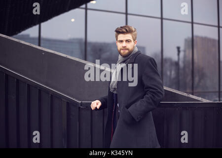 A photo of young, fashionable man wearing a shawl and coat. He's posing to the photo. Stock Photo