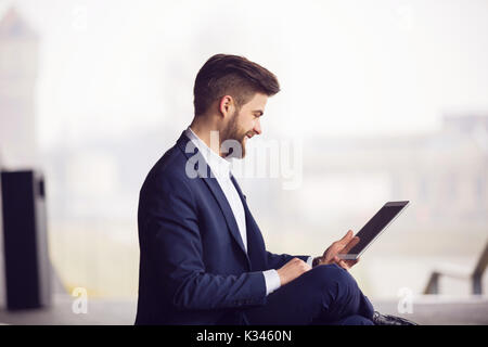 A photo of young, handsome businessman using tablet and smiling. Stock Photo