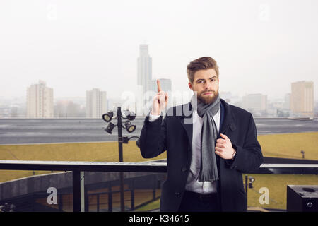 A photo of young, handsome man standing somewhere outside against urban background. He looks very seriously. Stock Photo