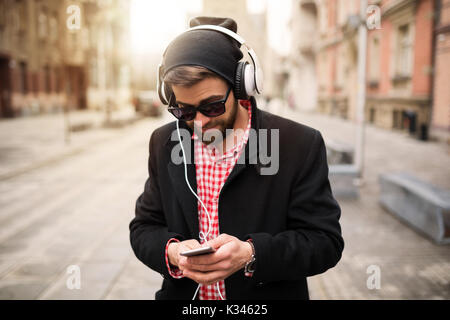 A photo of young, trendy man listening to the music through headphones and texting. Stock Photo