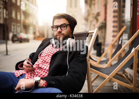 A photo of young man relaxing on the deckchair in front of some cafe. Stock Photo