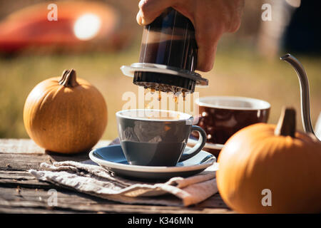 Man brewing filter coffee outdoor, at the autumn coffee picnic, on the old damaged wooden table background. Coffee drips captured in motion in the pro Stock Photo