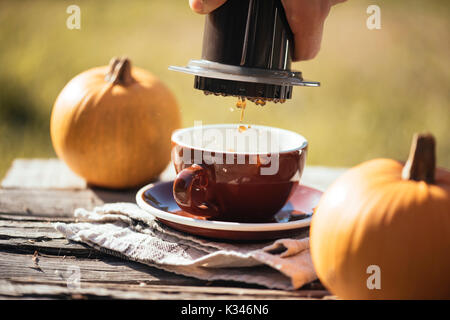 Man brewing filter coffee outdoor, at the autumn coffee picnic, on the old damaged wooden table background. Coffee drips captured in motion in the pro Stock Photo