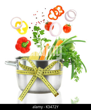 Fresh vegetables falling into a casserole pot with measuring tape Stock Photo