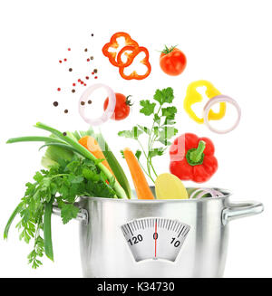 Fresh vegetables falling into a casserole pot with weight scale Stock Photo