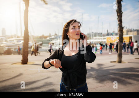 A photo of young, beautiful woman on the boulevard at the resort. She's talking on the mobile and waiting for someone. Stock Photo