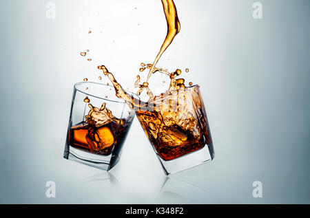 Two whiskey glasses clinking together on gray Stock Photo
