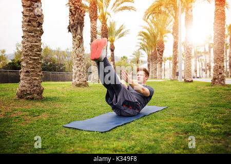 A photo of young, sporty man doing exercising at the park. He's keeping his hands and legs up. Stock Photo