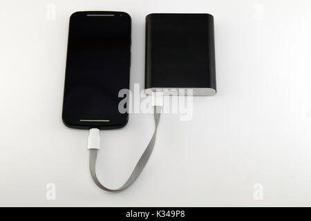 Smartphone charging from black power bank isolated on white background. Smartphone and power bank concept. Stock Photo