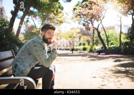 A photo of young, handsome man sitting on the bench at the park and resting against his knees. Stock Photo