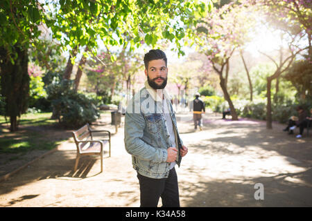 A photo of young, handsome man standing on the alley in the park. He's wearing denim jacket. Stock Photo