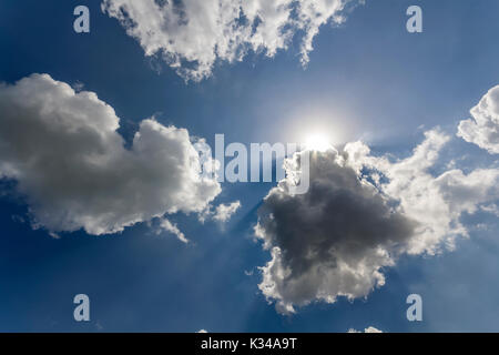 Rays of sun shining through white puffy clouds and blue sky Stock Photo
