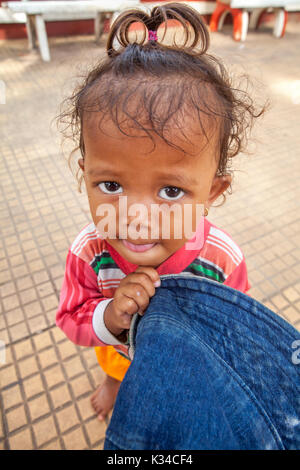 A cute young child with a blue hat and imploring eyes begs on a sidewalk in Siem Reap, Cambodia. Stock Photo