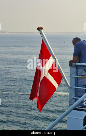 Danish flag hoisted on the flagpole of a ferry in the evening with the calm sea in the background Danish flag hoisted on the flagpole of a ferry in the evening with the calm sea in the background
