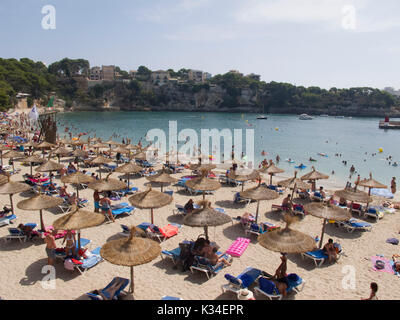Tourists relax under beach umbrellas in Porto Christo Stock Photo