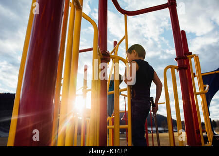 A boy plays on playground equipment at sunset. Stock Photo