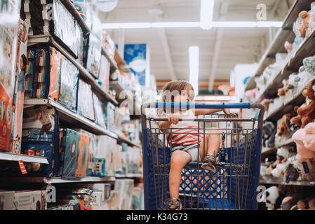 A toddler sits in a shopping cart in a toy store. Stock Photo