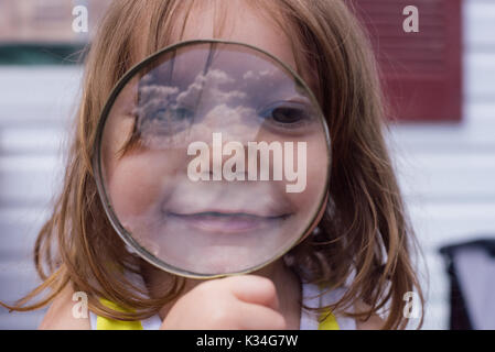A young girl looks through a circular magnifying glass. Stock Photo