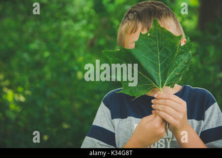 A young boy holds a green leaf in front of his face. Stock Photo