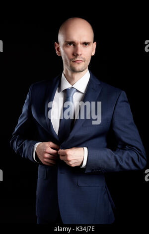 Portrait of serious businessman fastens his jacket. Studio shot on black background. Stock Photo