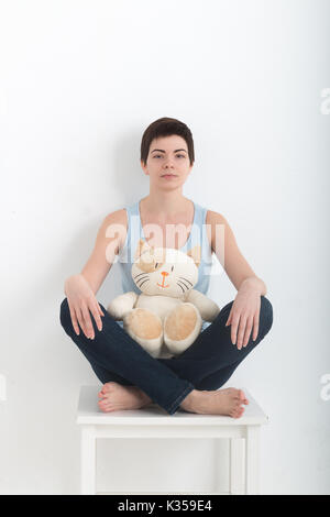 Young attractive smiling woman practicing yoga, sitting in Half Lotus exercise Ardha Padmasana pose, working out wearing dark bleu jeans indoor full l Stock Photo