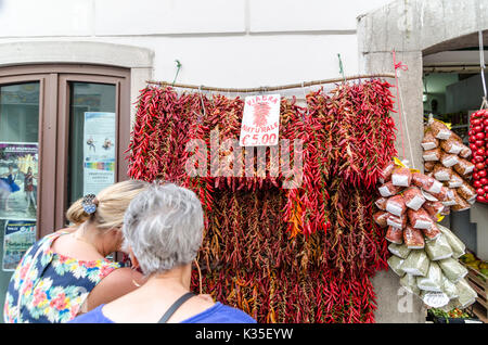 Two women looking at dried and fresh chillies strung up outside a shop with 'Natural Viagra' sign in Amalfi, Italy. Stock Photo