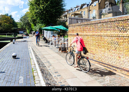 Two cyclists on the towpath of Regent's Canal, Islington, London, UK, people sitting outside at a canalside cafe Stock Photo