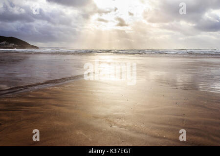 Backlit image of a cloudy sky and evening sun reflecting on the sandy beach at low tide, Westward Ho!, Devon, England, UK Stock Photo