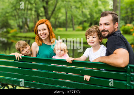 Happy family sitting on bench in park Stock Photo