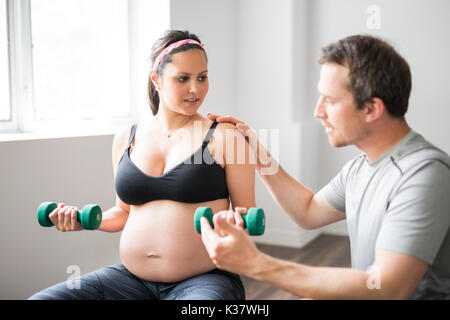 Pregnant woman working out with dumbbells with personal trainer at the gym Stock Photo