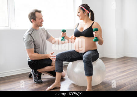 Pregnant woman working out with dumbbells with personal trainer at the gym Stock Photo