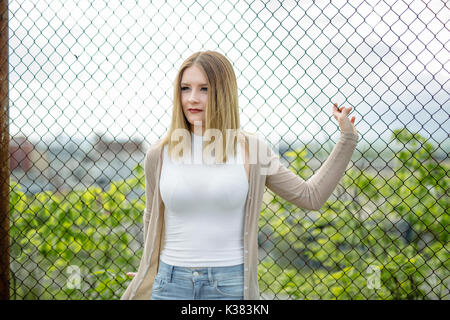 Closeup of pretty young woman standing near chain link fence Stock Photo