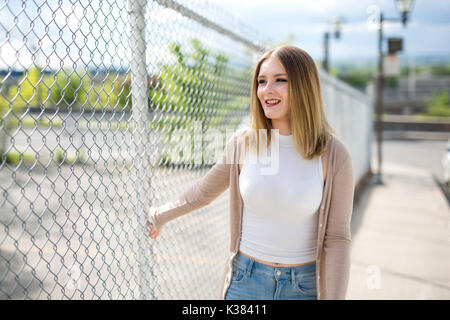 pretty young woman standing near chain link fence Stock Photo