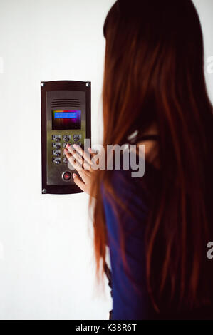 attractive woman in a blue elegant dress, dials code into intercom, at entrance of house Stock Photo