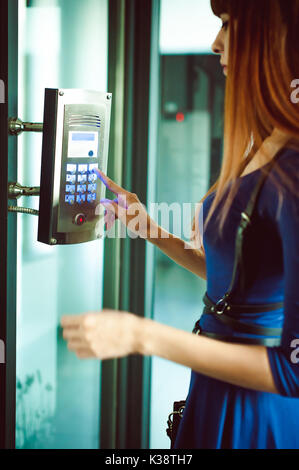 attractive woman in a blue elegant dress, dials code into intercom, at entrance of house Stock Photo