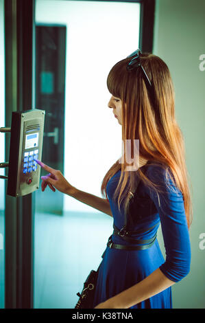 attractive woman in a blue elegant dress, dials code into intercom, at entrance of house Stock Photo