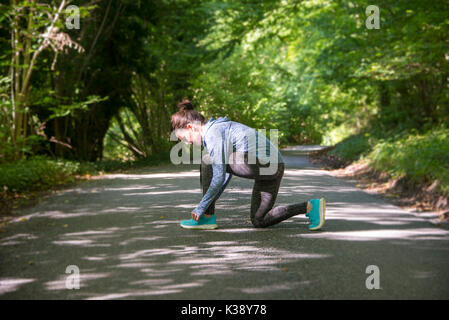 woman jogger doing up her shoelaces getting ready to run on a country road Stock Photo