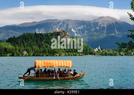 Traditional Pletna boat with colorful canopy on Lake Bled with Bled castle on cliff and St Martin church Sol massive of Karavanke mountains Slovenia Stock Photo