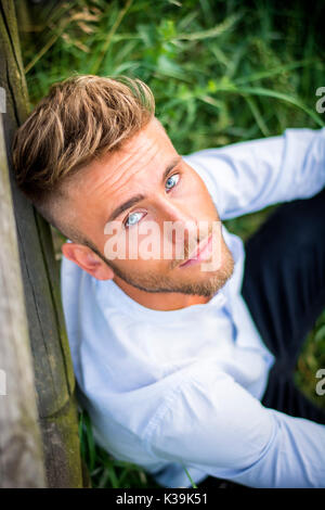Blondish, blue eyed young man on wood fence Stock Photo