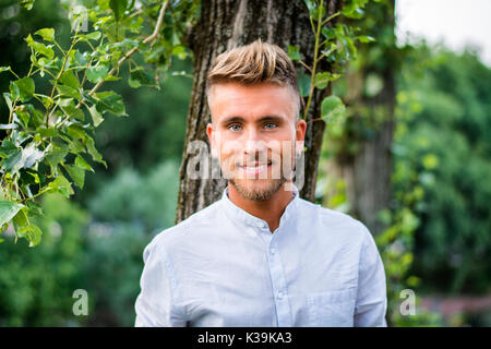 Sad, worried blond young man against tree Stock Photo