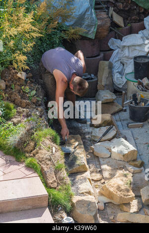 Man Build a dry wall in the garden. In the background, various tools. Stock Photo