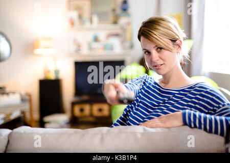 Young beautiful woman watching TV on a sofa at home Stock Photo