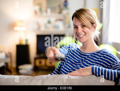 Young beautiful woman watching TV on a sofa at home Stock Photo