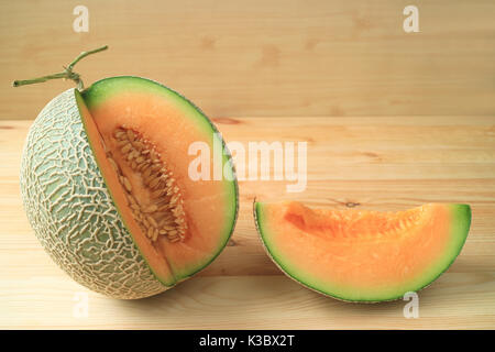 Fresh ripe muskmelon sliced from the whole fruit isolated on a wooden table Stock Photo
